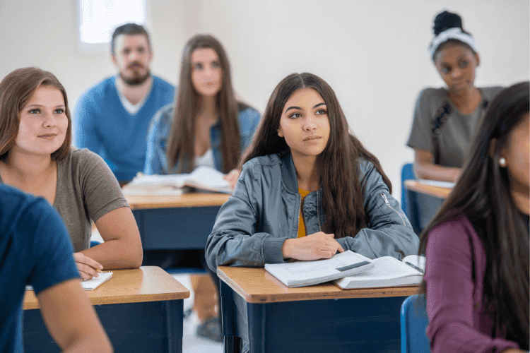 Group of high school students sitting at desks, listening attentively during a classroom lesson.