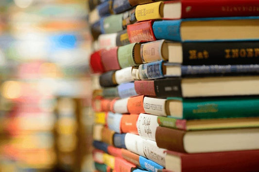Large stack of assorted hardcover and paperback books arranged in a vertical pile.