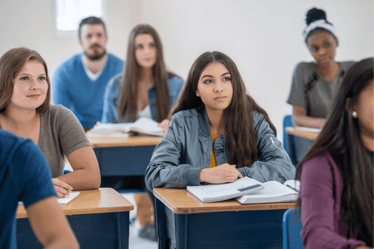 Group of high school students sitting at desks, listening attentively during a classroom lesson.